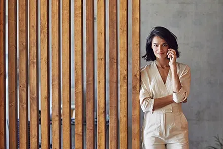 Telefonierende Frau neben einer Holzwand, BFS finance GmbH