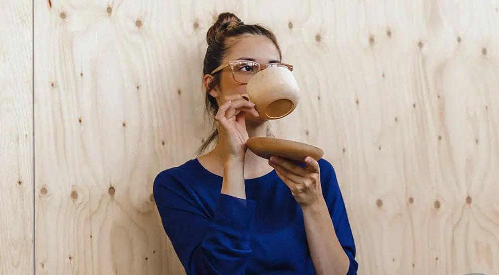 Frau trinkt an einer Holzwand gelehnt Kaffee
